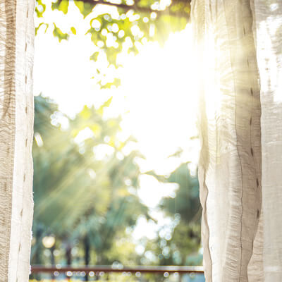 Bild på ett öppet fönster med solljus som strilar in genom vita gardiner.